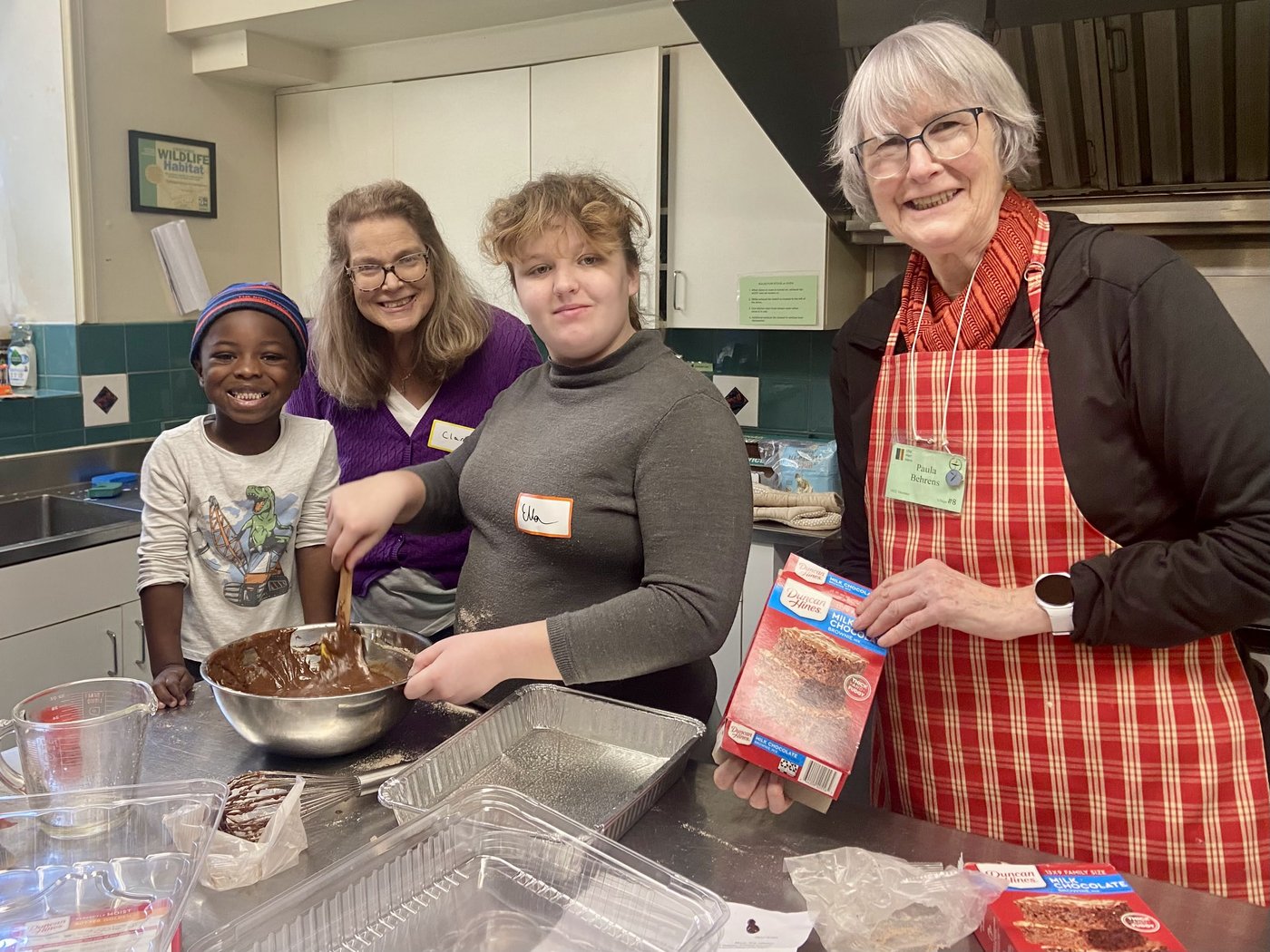 A child and volunteers mixing brownie batter together in the kitchen